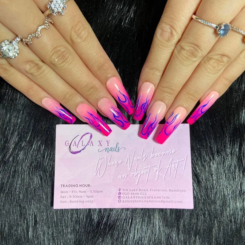 Long pink nails with purple flames, resting above the pink Galaxy Nails business card